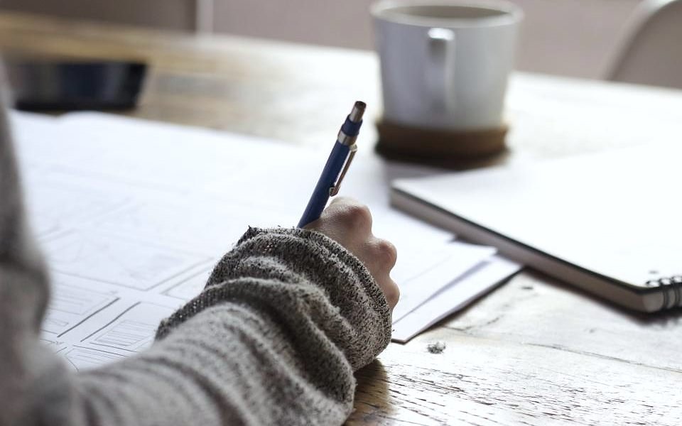 Açık defter üzerine not alan el ve kahve fincanı.