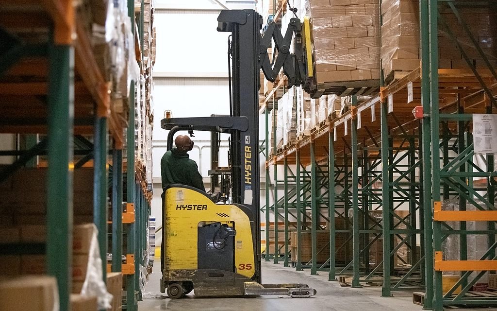 Depo raflarında paletli ürünleri taşıyan forklift.